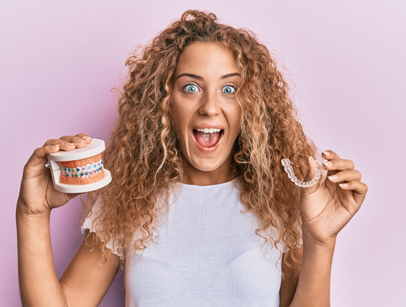 Young lady holding clear aligners, model teeth, and smiling.